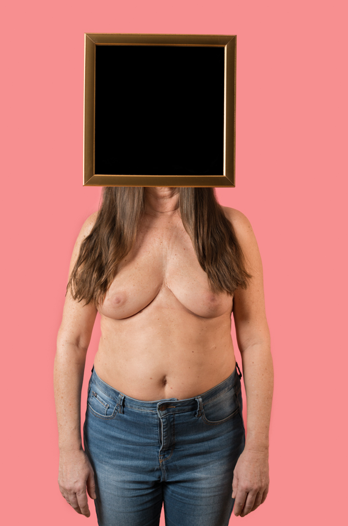Frau Oberkörper frei steht mit dem Gesicht hinter einem Spiegel.